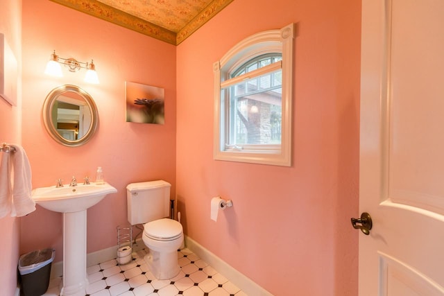 half bath featuring toilet, baseboards, and a sink