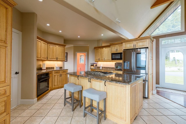 kitchen with dark stone counters, black appliances, light tile patterned flooring, and a kitchen island