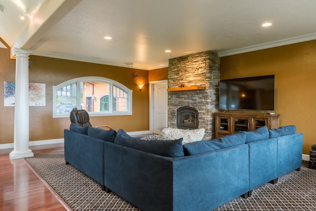 living area with crown molding, a stone fireplace, wood finished floors, and ornate columns