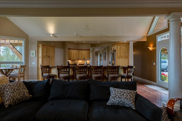 living area featuring a wealth of natural light, lofted ceiling, decorative columns, and wood finished floors