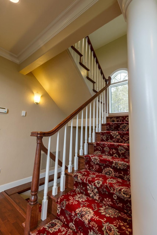 stairway with baseboards, wood finished floors, and crown molding