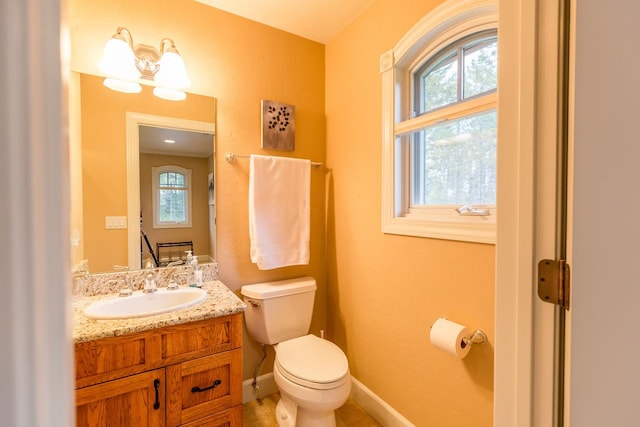 half bathroom featuring toilet, plenty of natural light, vanity, and baseboards