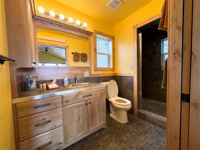 full bath featuring toilet, a wainscoted wall, visible vents, tile walls, and a shower stall