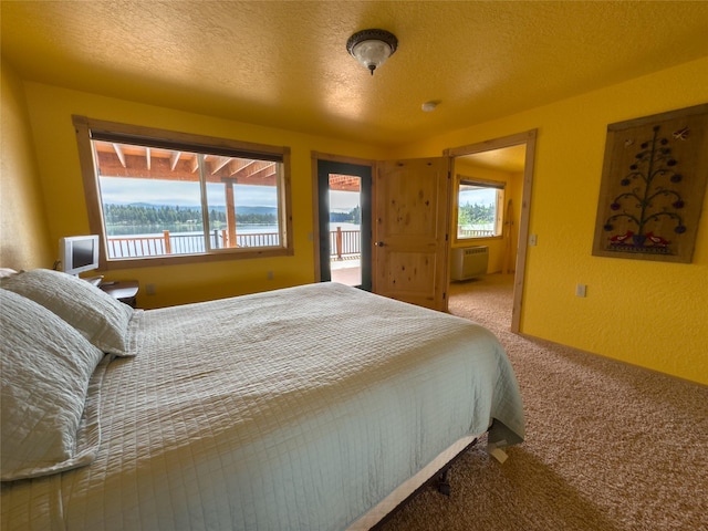 bedroom with a textured ceiling, multiple windows, carpet flooring, and an AC wall unit