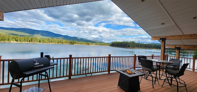 dock area featuring a fire pit, a deck with water view, and a wooded view