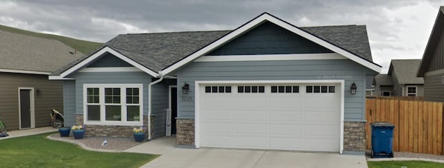 view of front of home with a garage, driveway, stone siding, and fence