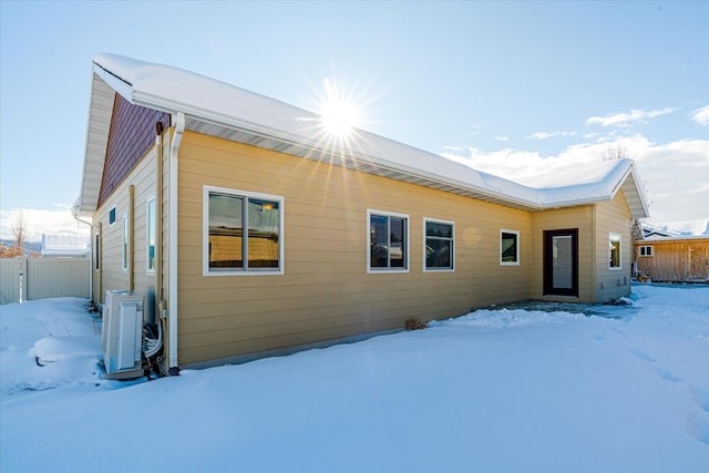 snow covered back of property with ac unit and fence