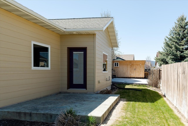 view of exterior entry featuring a patio, a shingled roof, fence, and a yard