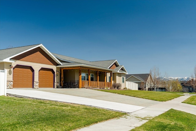 view of front of property with an attached garage, a front lawn, stone siding, concrete driveway, and covered porch