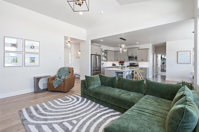 living area featuring baseboards, high vaulted ceiling, light wood-style floors, and recessed lighting