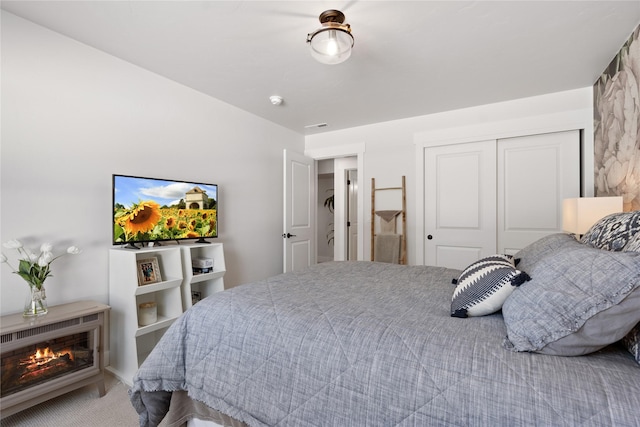 carpeted bedroom with a warm lit fireplace, a closet, and visible vents