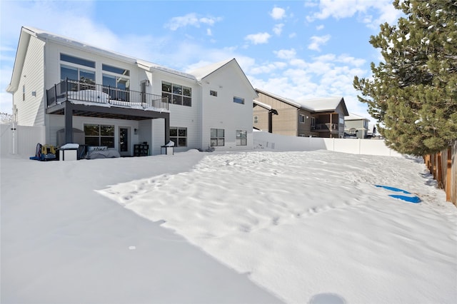 snow covered back of property with a fenced backyard and a balcony