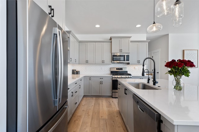 kitchen with a sink, light wood finished floors, appliances with stainless steel finishes, a kitchen island with sink, and decorative backsplash