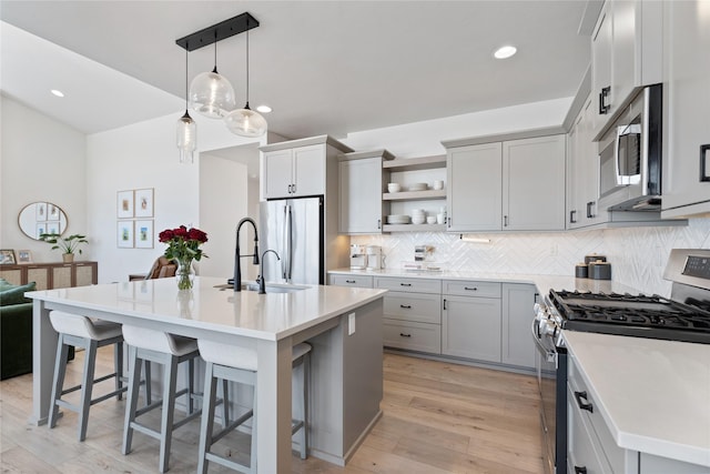 kitchen featuring appliances with stainless steel finishes, open shelves, light wood-style floors, a breakfast bar area, and backsplash