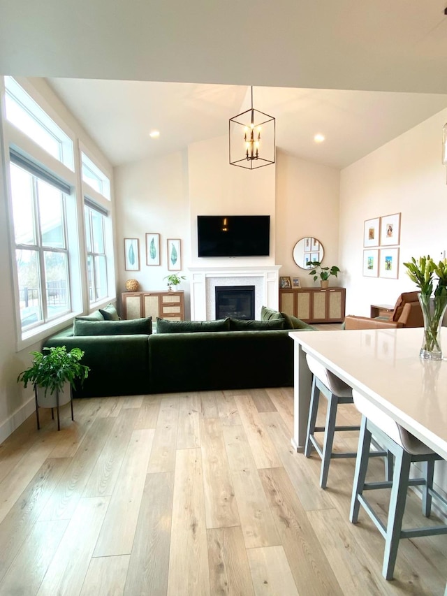 living room with lofted ceiling, light wood-style flooring, a glass covered fireplace, and a notable chandelier