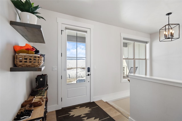 doorway to outside featuring light wood finished floors, baseboards, and a chandelier