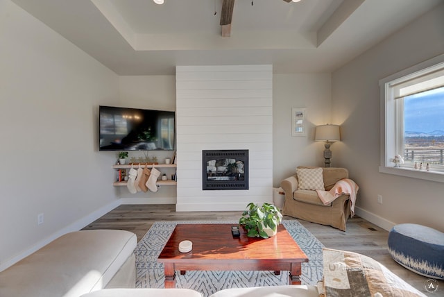 living area featuring ceiling fan, a fireplace, wood finished floors, and baseboards