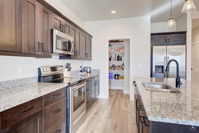 kitchen featuring light stone counters, stainless steel appliances, a sink, and decorative light fixtures