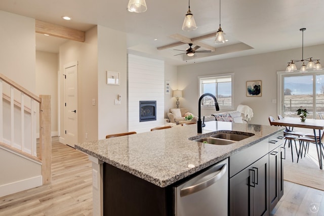 kitchen featuring a center island with sink, dishwasher, open floor plan, hanging light fixtures, and a sink