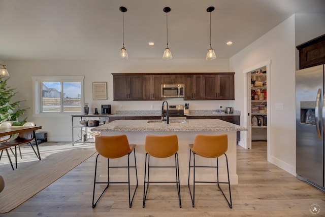 kitchen featuring dark brown cabinetry, a center island with sink, stainless steel appliances, and a sink