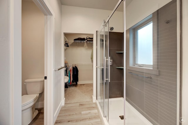 full bath featuring a spacious closet, toilet, a stall shower, wood finished floors, and baseboards