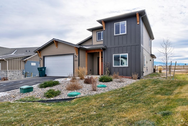 view of front of property featuring aphalt driveway, board and batten siding, a front yard, fence, and a garage