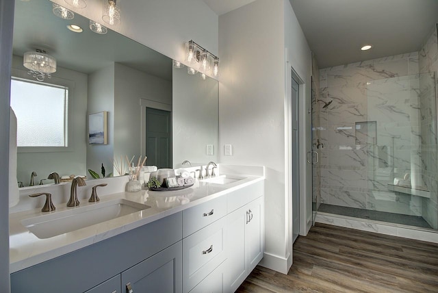 bathroom with double vanity, a marble finish shower, a sink, and wood finished floors