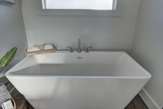 full bath featuring a freestanding bath, wood finished floors, and baseboards