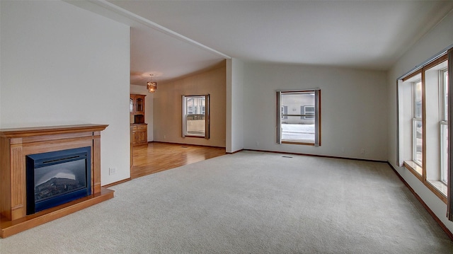 unfurnished living room featuring vaulted ceiling, light carpet, a glass covered fireplace, and baseboards