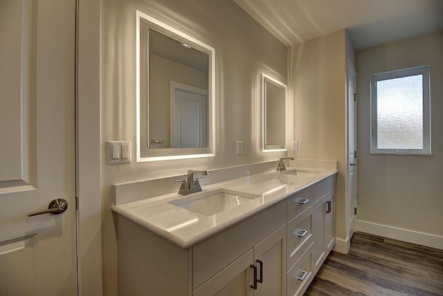 bathroom with double vanity, wood finished floors, a sink, and baseboards