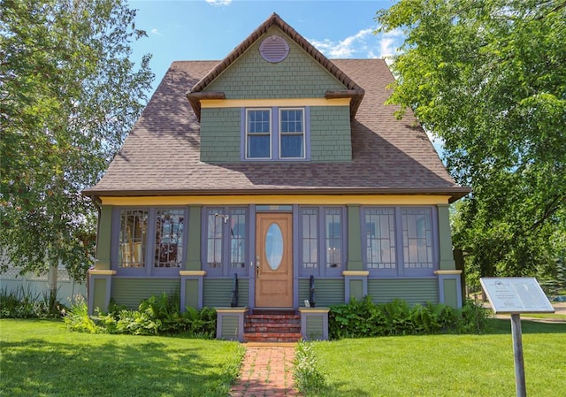 view of front of home with entry steps, a shingled roof, and a front yard