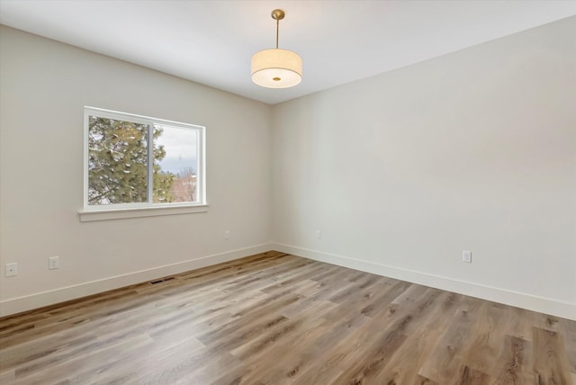 empty room with light wood-style floors, visible vents, and baseboards