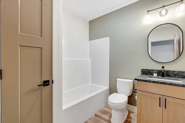 bathroom with baseboards, toilet, vanity, wood finished floors, and shower / bathtub combination