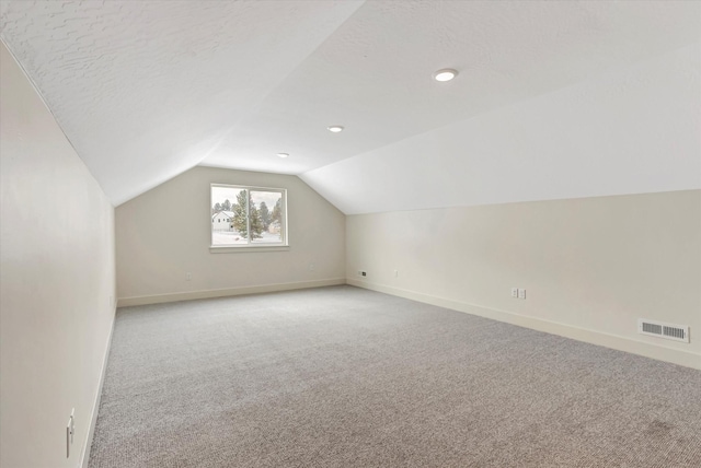 additional living space featuring light carpet, baseboards, visible vents, and vaulted ceiling