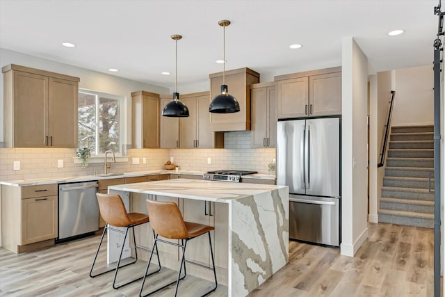 kitchen with a sink, a kitchen island, appliances with stainless steel finishes, light brown cabinetry, and pendant lighting