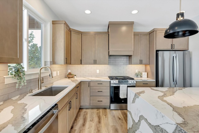 kitchen featuring wall chimney exhaust hood, appliances with stainless steel finishes, decorative light fixtures, light brown cabinets, and a sink