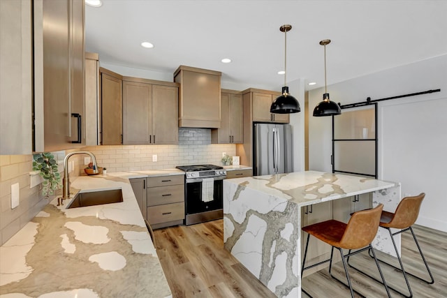 kitchen featuring a barn door, a kitchen island, appliances with stainless steel finishes, premium range hood, and a sink