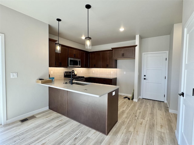 kitchen featuring a sink, a peninsula, stainless steel microwave, backsplash, and visible vents