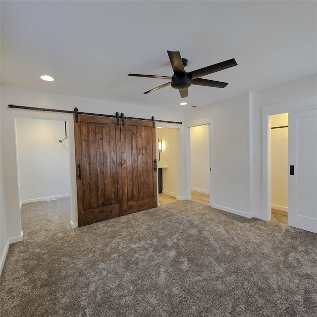 unfurnished bedroom with light carpet, a barn door, baseboards, and recessed lighting