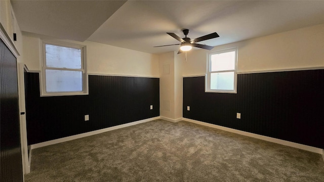 unfurnished room featuring dark colored carpet, wainscoting, ceiling fan, wooden walls, and baseboards