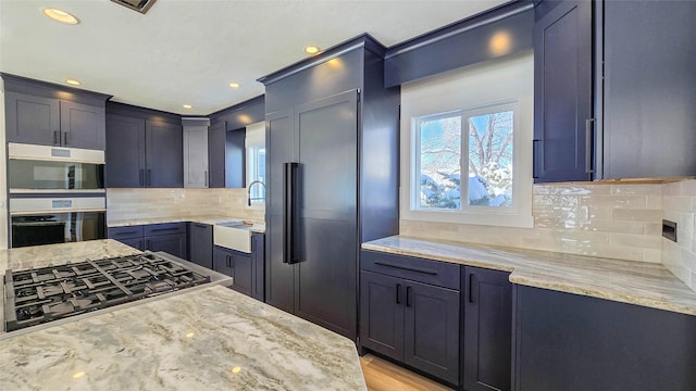 kitchen featuring stainless steel gas cooktop, light stone counters, a sink, and tasteful backsplash