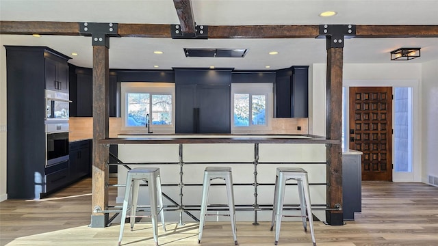 kitchen featuring a wealth of natural light, stainless steel oven, a kitchen bar, and wood finished floors