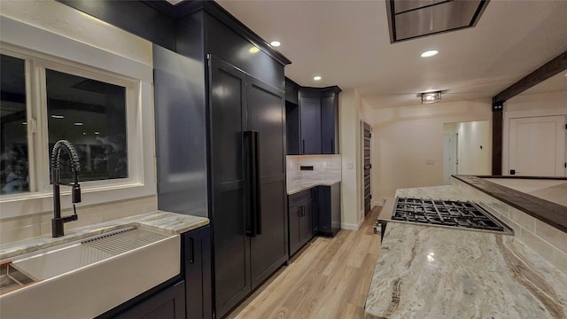 kitchen featuring paneled refrigerator, dark cabinets, a sink, light stone countertops, and tasteful backsplash