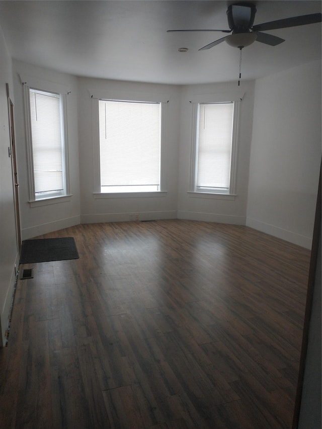 unfurnished room with dark wood-style floors, visible vents, baseboards, and a ceiling fan