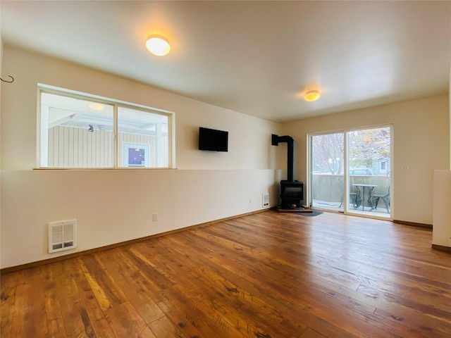 unfurnished living room featuring a wood stove, visible vents, baseboards, and wood finished floors