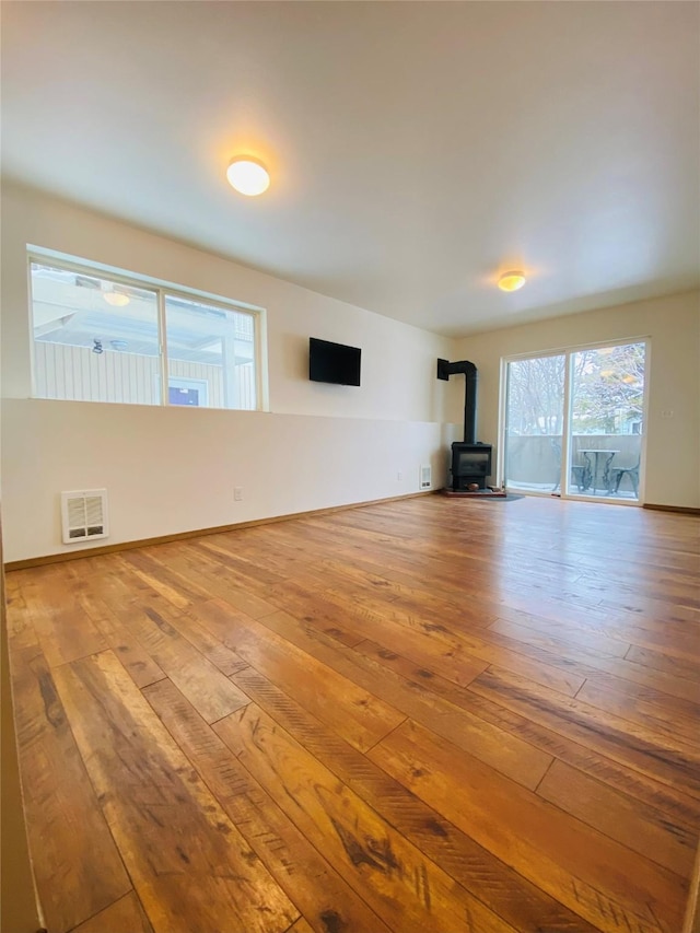 unfurnished living room featuring light wood-type flooring, a wood stove, visible vents, and baseboards