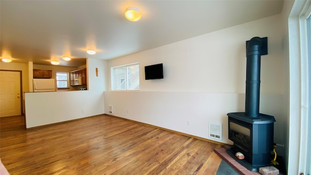 unfurnished living room with a wood stove, light wood-style flooring, and visible vents