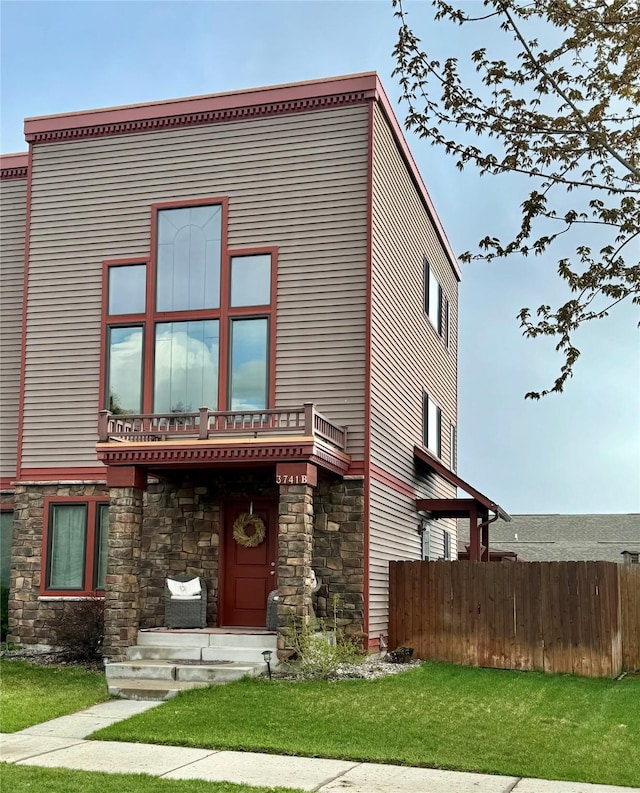 view of front of house with stone siding, fence, and a front yard