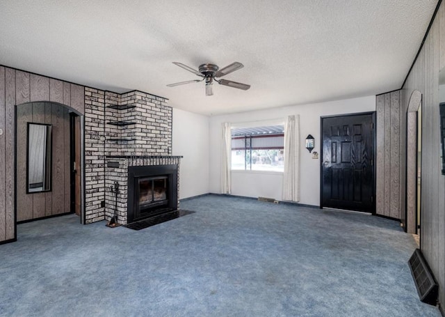 3501 1st Ave S, Great Falls, MT 59401 - unfurnished living room featuring a textured ceiling, ceiling fan, a brick fireplace, carpet floors, and wood walls