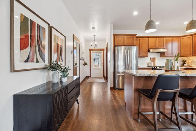 kitchen with freestanding refrigerator, brown cabinets, hanging light fixtures, and under cabinet range hood